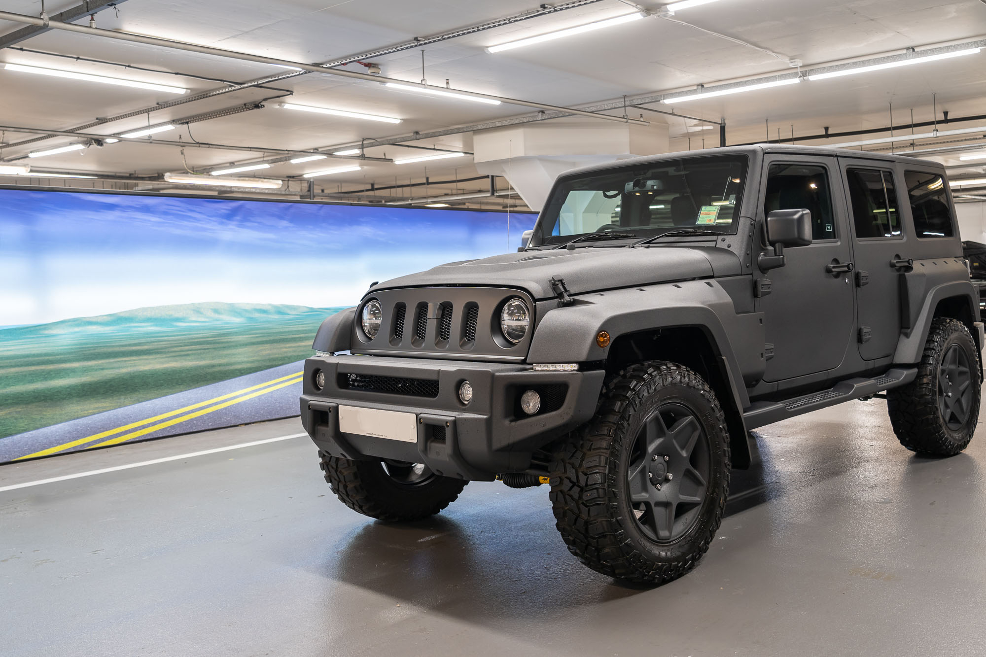 Matt grey Jeep Wrangler with black alloy wheels parked in a valeting bay