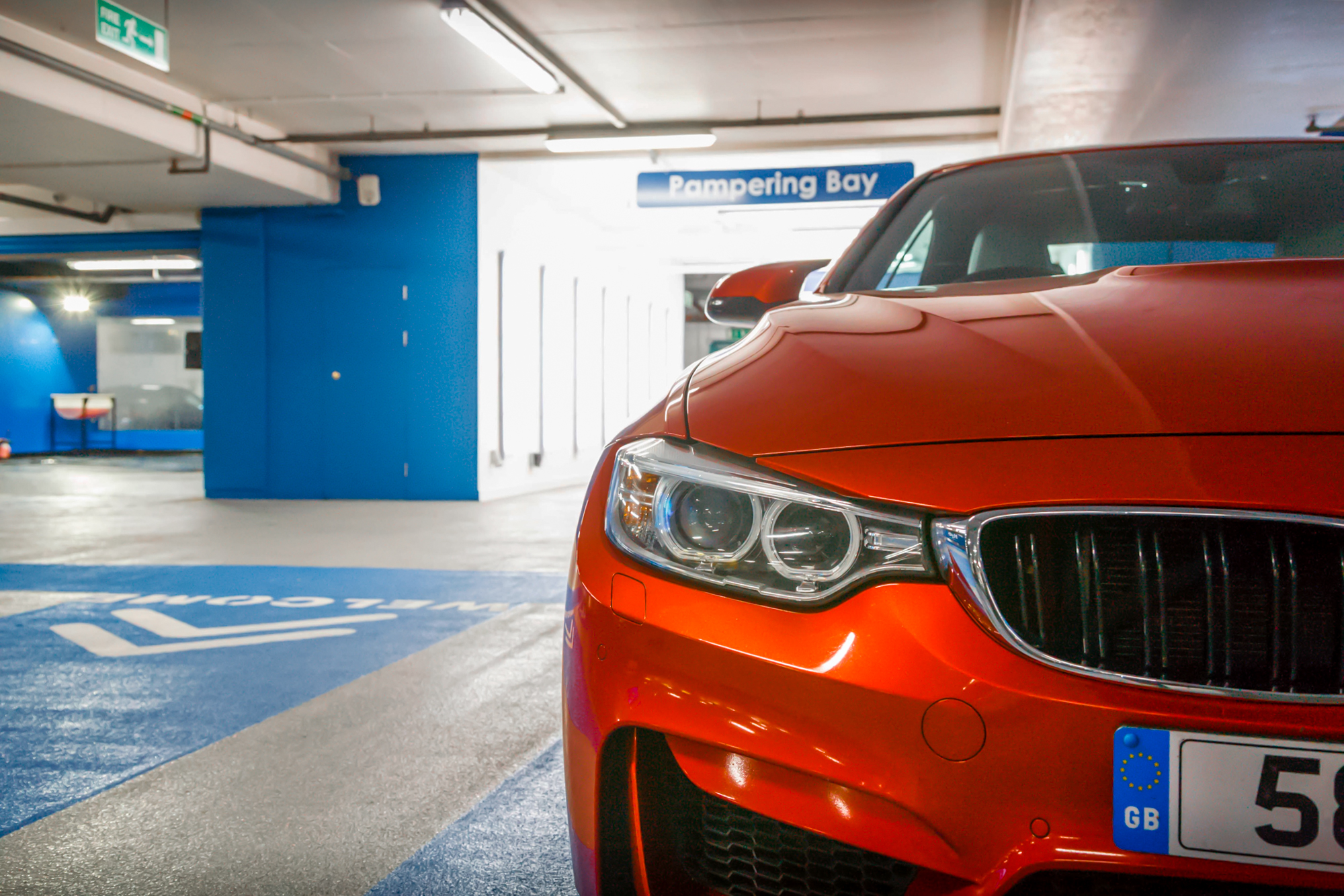 Front of an orange BMW in a car park bay marked Pampering Bay