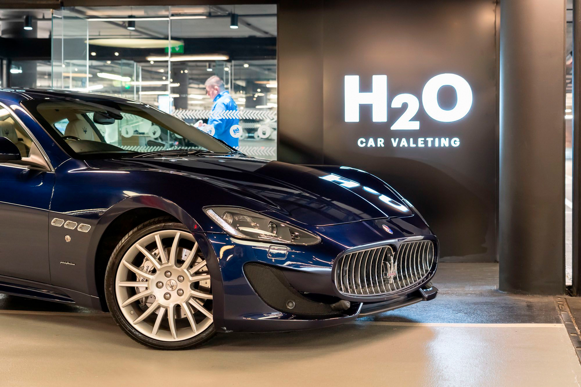 Front of a dark blue Maserati beside an illuminated H2O Car Valeting sign