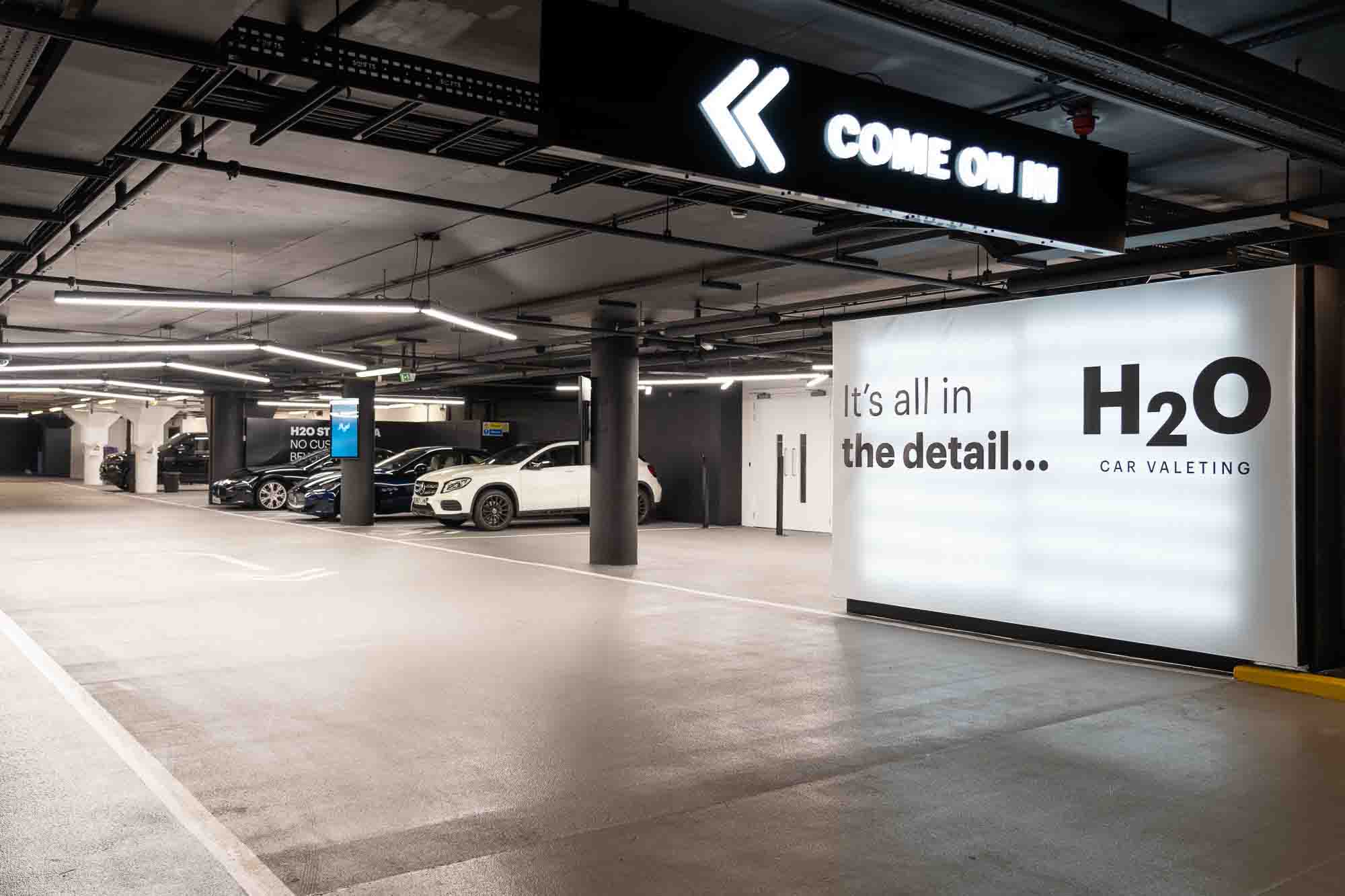 Illuminated "Come on in" sign and H2O Car Valeting wall in a parking-level valeting bay